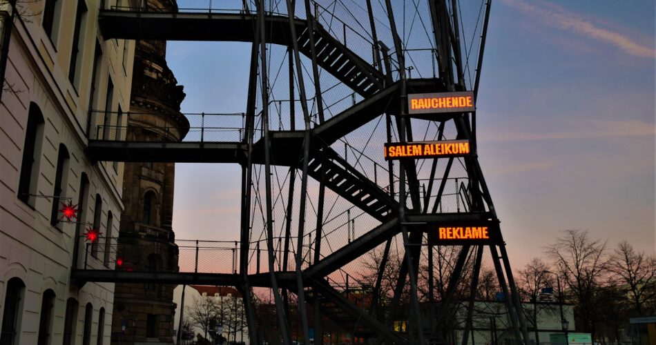 Eine Installation an der Fluchttreppe des Landhauses zeigt in drei LED-Panels untereinander die Worte "RAUCHENDE/ SALEM ALEIKUM / REKLAME". Die Worte leuchten rot und bewegen sich.