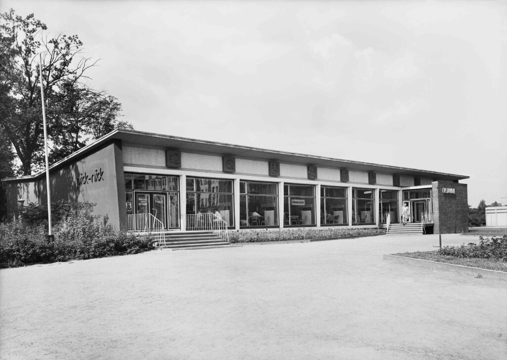 Der Schrägblick auf das pick-nick zeigt einen langgezogenen Pavillonbau mit Schmetterlingsdach und großen Schaufenstern.