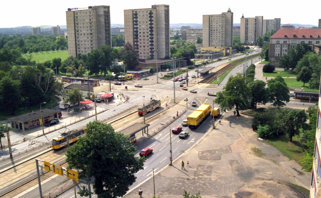 Blick von oben auf den Fučikplatz mit breiter Straße und Straßenbahn. Im Hintergrund Hochhäuser und davor die drei Pavillonbauten.