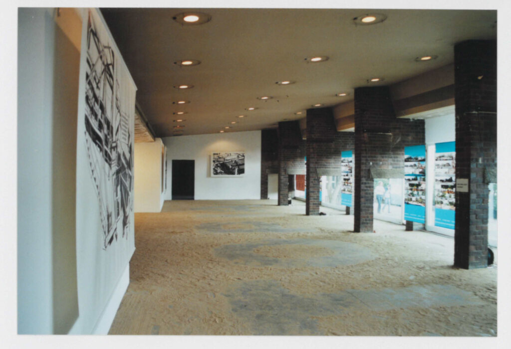 Für die Ausstellung wurde der Boden des Raums mit Sand bestreut, in den Buchstaben gekehrt wurden. Vor den Fenstern und an den Wänden Kunstwerke.