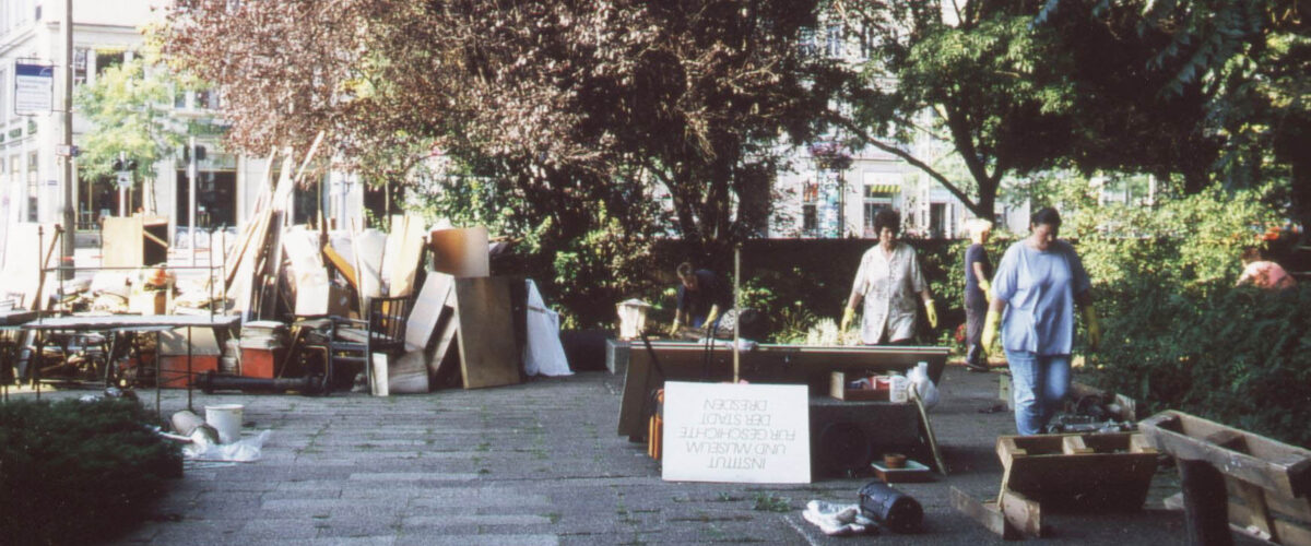 Vor dem landhaus stapelt sich Sperrmüll, Frauen mit Gummihandschuhen gehen an einem abgestellten Schild mit der Aufschrift "Institut und Museum für Geschichte der Stadt Dresden"