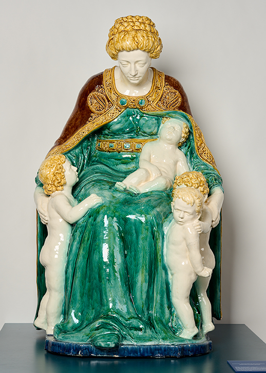 Figur aus Steingut – Eine sitzende Frau mit grünem Kleid und rotem Umhang mit goldenen Stadtwappen hat vier Putten um sich geschart.