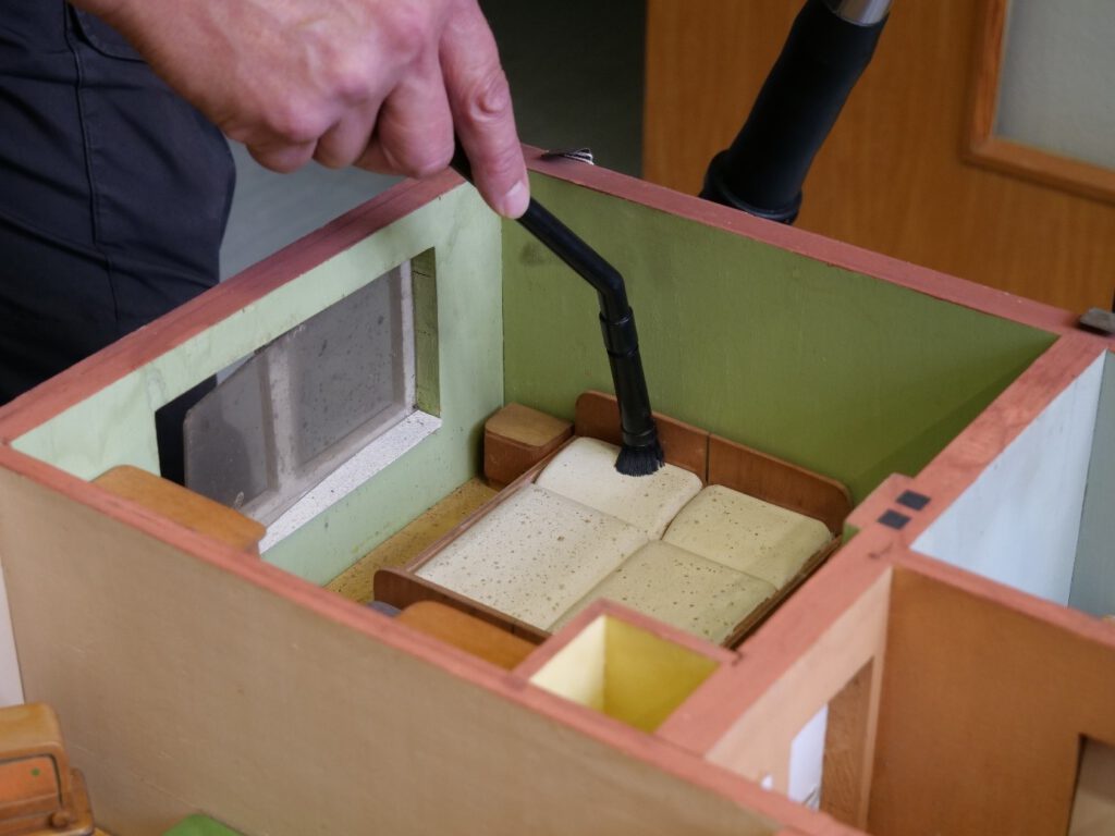 Das Schlafzimmer eines Hausmodells wird mit kleiner Staubsaugerdüse und Pinsel gereinigt.