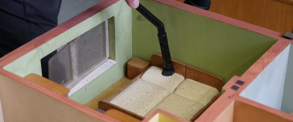 Das Schlafzimmer eines Hausmodells wird mit kleiner Staubsaugerdüse und Pinsel gereinigt.