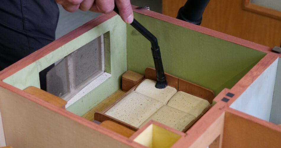Das Schlafzimmer eines Hausmodells wird mit kleiner Staubsaugerdüse und Pinsel gereinigt.